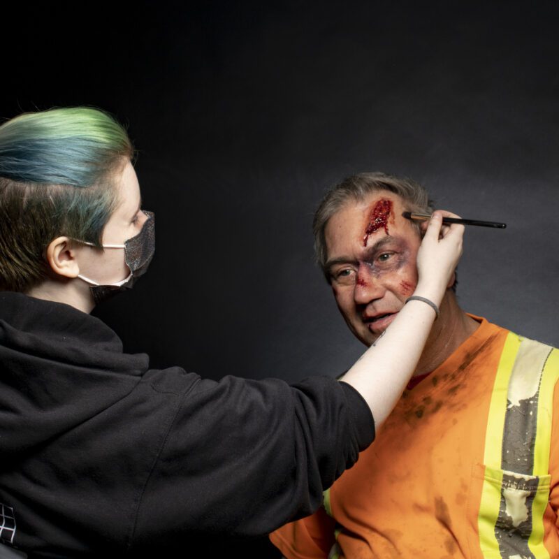A CMU student adding makeup to a man during a class